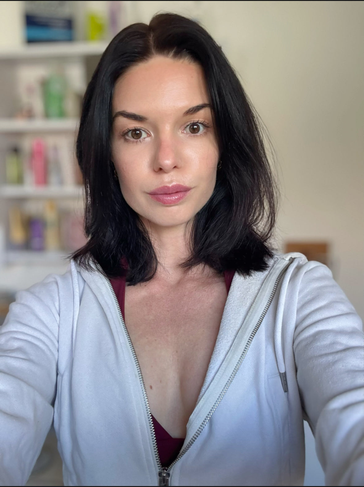 Woman wearing a white zip-up hoodie in a room with shelves in the background