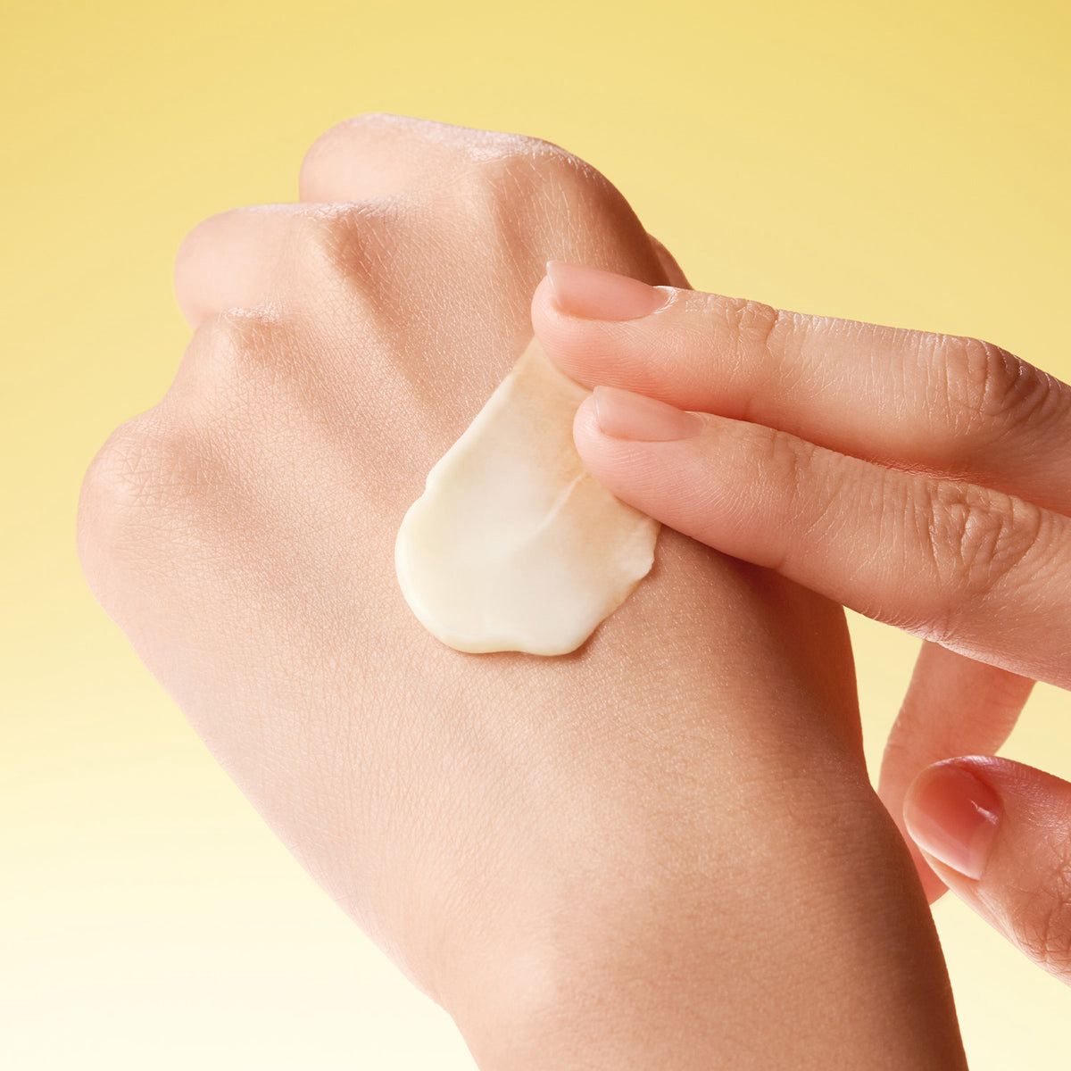 Hand applying cream to another hand against a yellow background